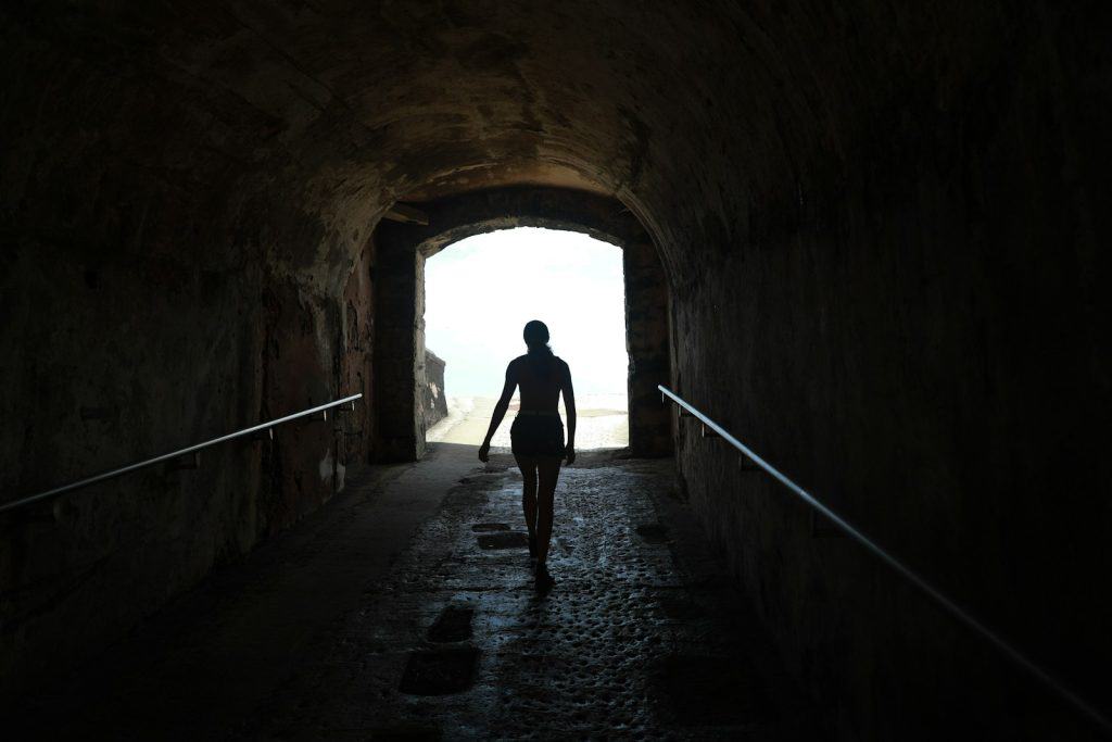 Silhouette of a person walking through a dark tunnel towards bright light, symbolizing the journey of healing and recovery from eating disorders at Serengeti Wellness.