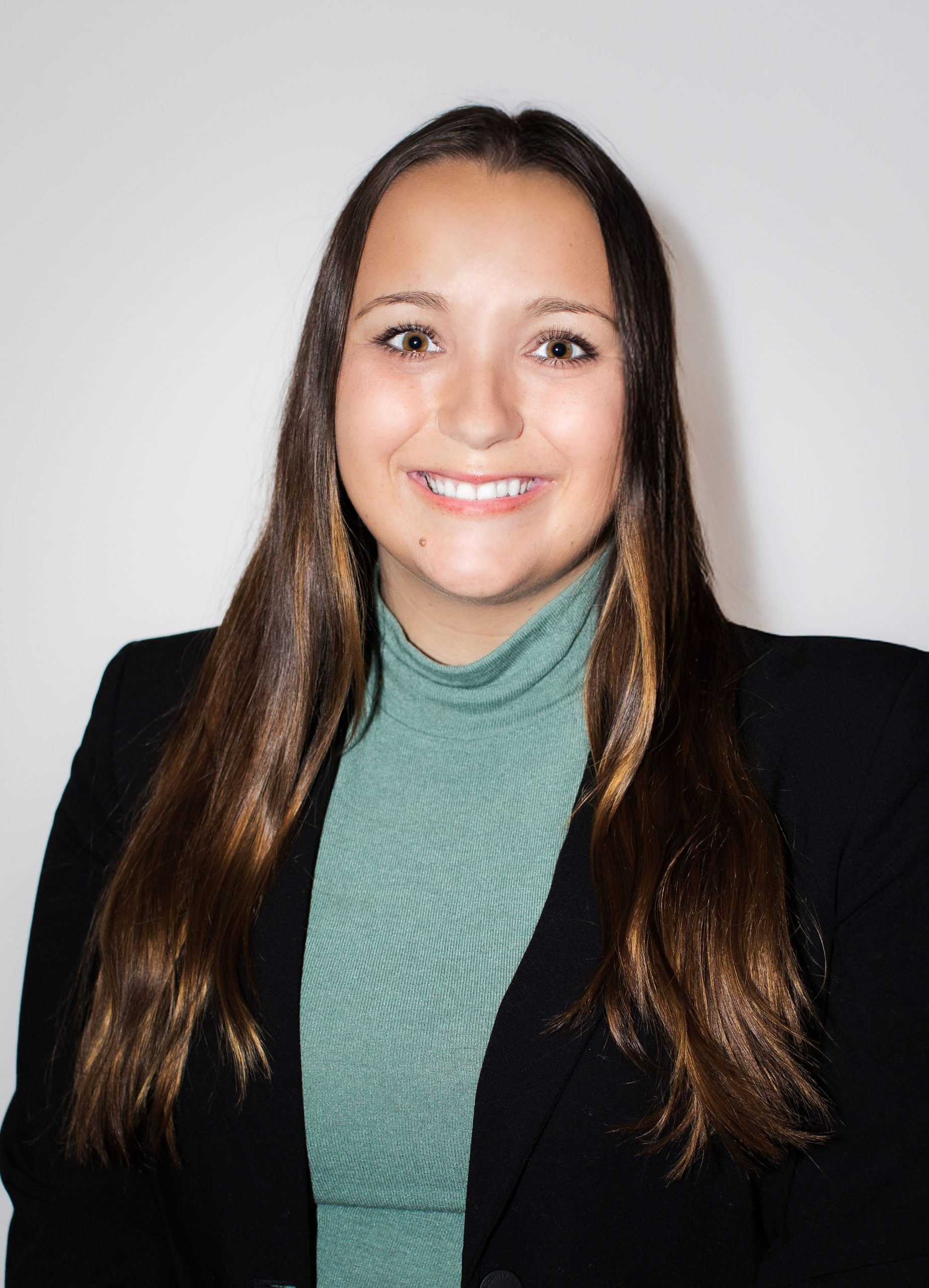 Young woman in a green turtleneck and black blazer, representing Serengeti Wellness for BIPOC mental health therapy.