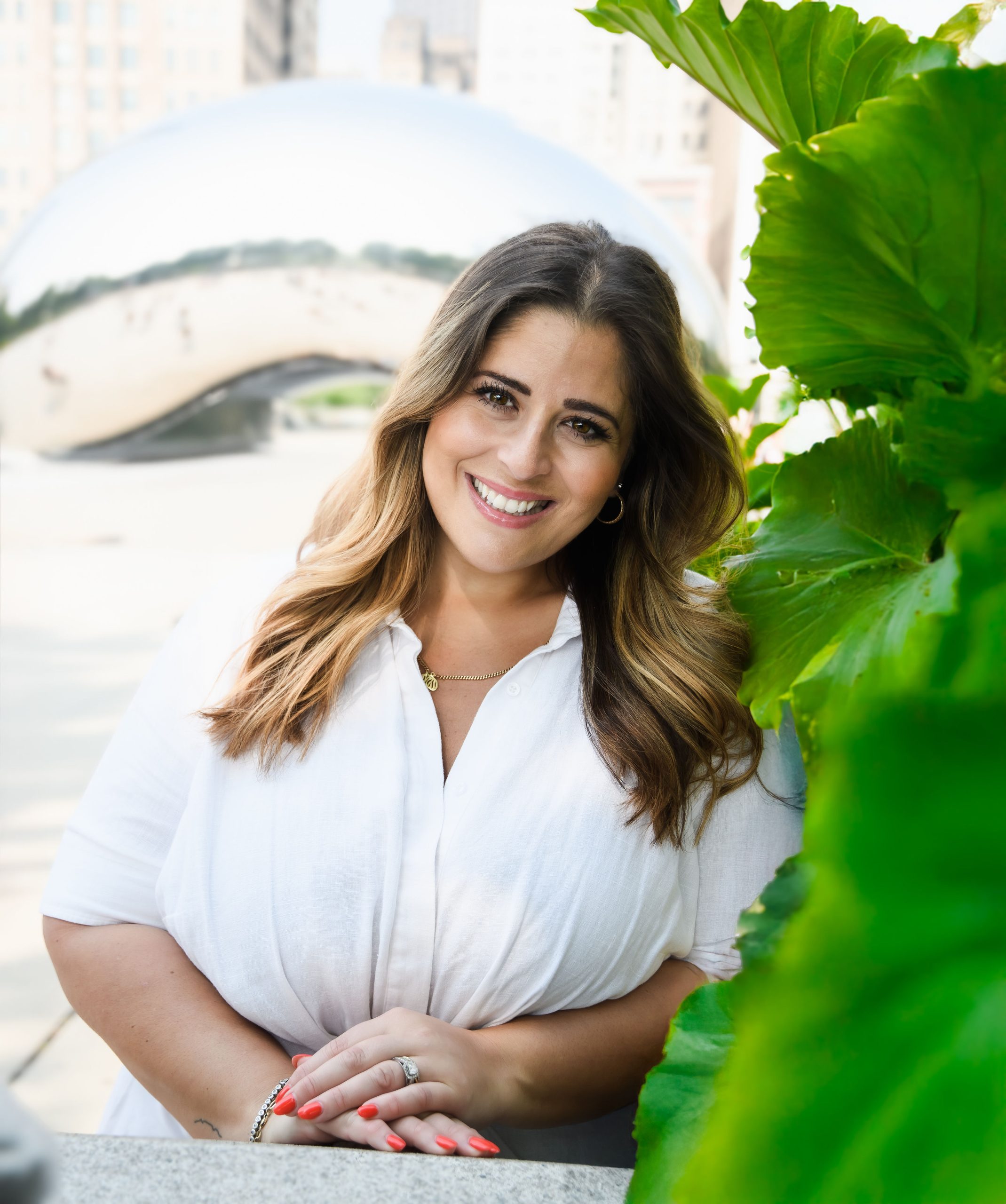 Carla da Cunha, psychotherapist at Serengeti Wellness, smiling outdoors with greenery and the Chicago Bean sculpture in the background.