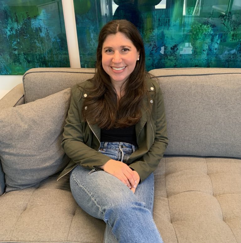 Licensed therapist Jona Koplow sitting on a gray couch, smiling, in a supportive environment focused on mental health and grief counseling.