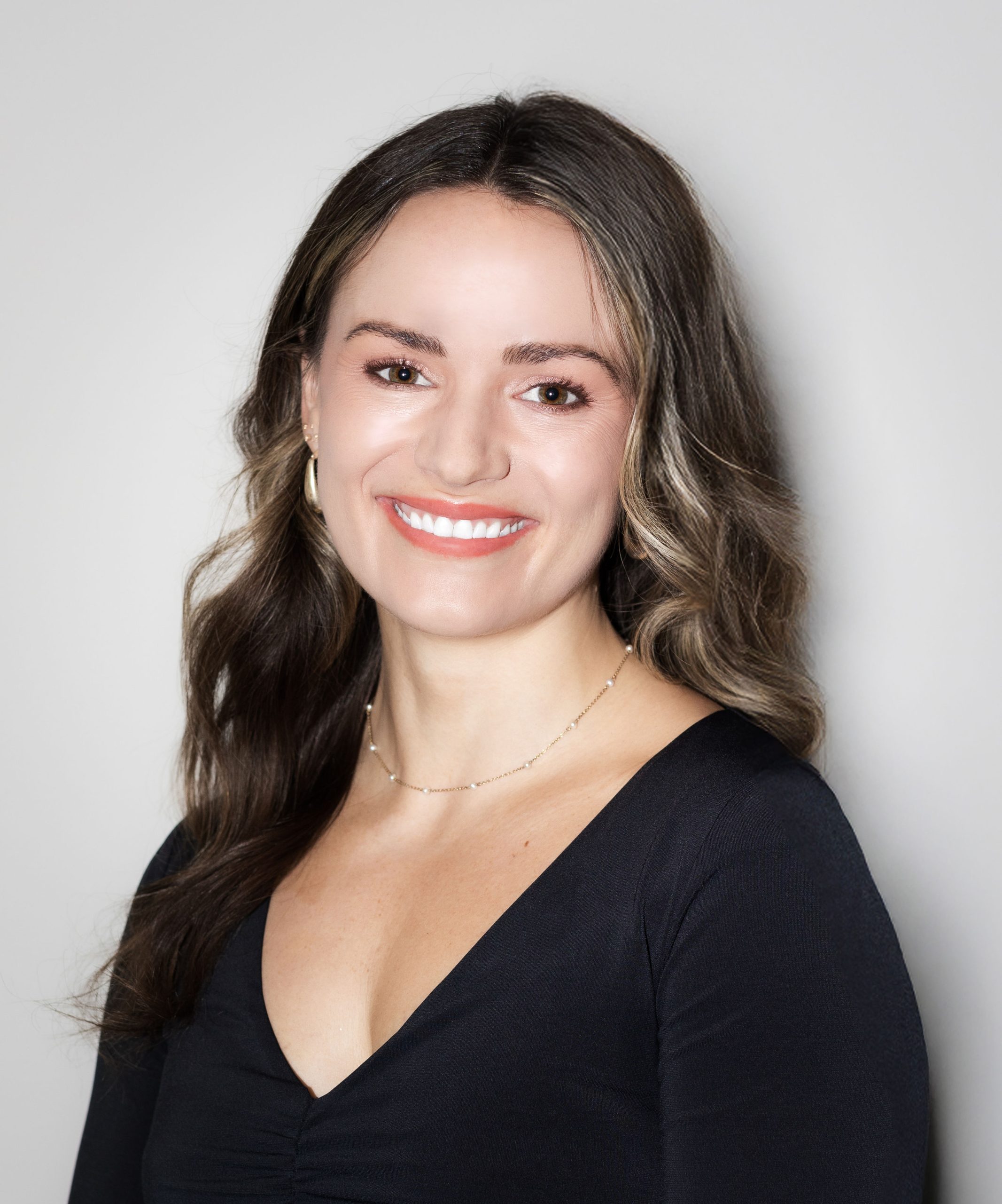 A woman with long, wavy hair smiles in a black fitted top, showcasing Serengeti Wellness&rsquo;s focus on BIPOC mental health.