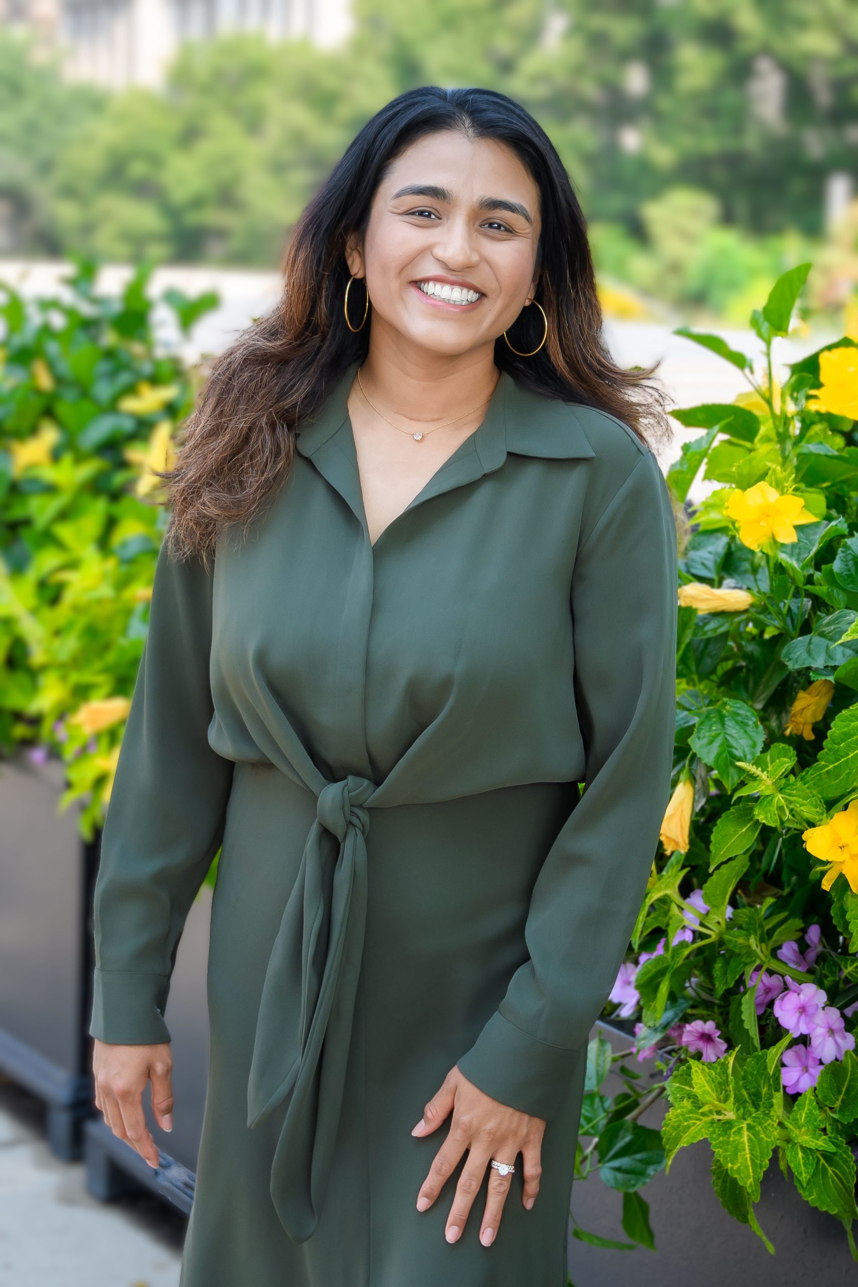 Olivia DeLeon-Yi, LCSW, MSW, smiling in a green blouse, standing among vibrant flowers, representing Serengeti Wellness's diverse therapy team.