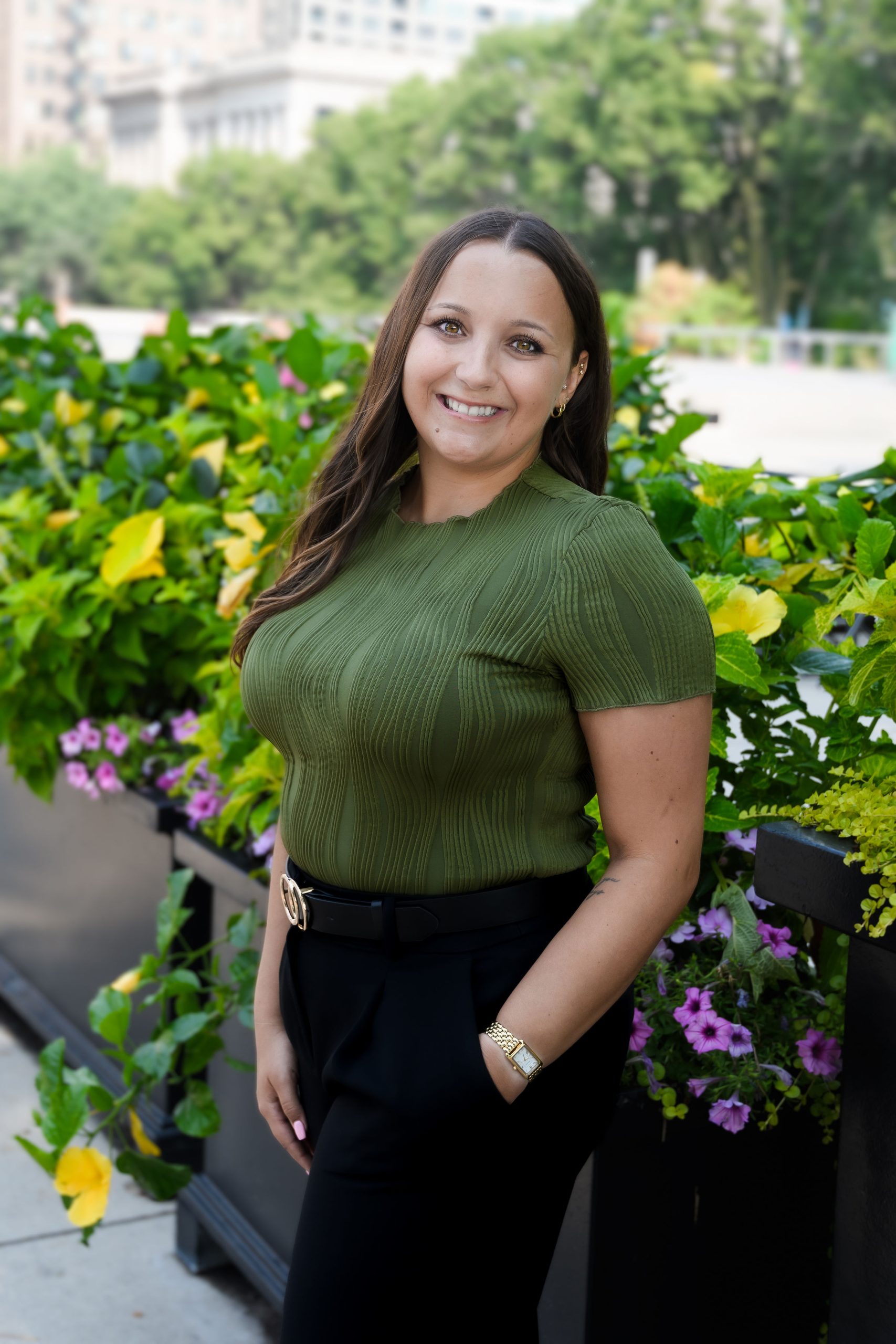 Alyssa Meixelsperger, therapist at Serengeti Wellness, smiling in a green top against a backdrop of vibrant flowers, representing a holistic approach to mental health.